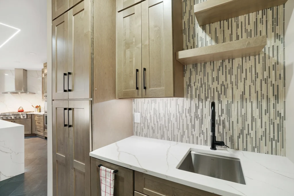 Modern kitchen sink area with light wood cabinets, marble countertop, open shelves, mosaic tile backsplash, and a black faucet. A towel hangs from a handle below the counter.