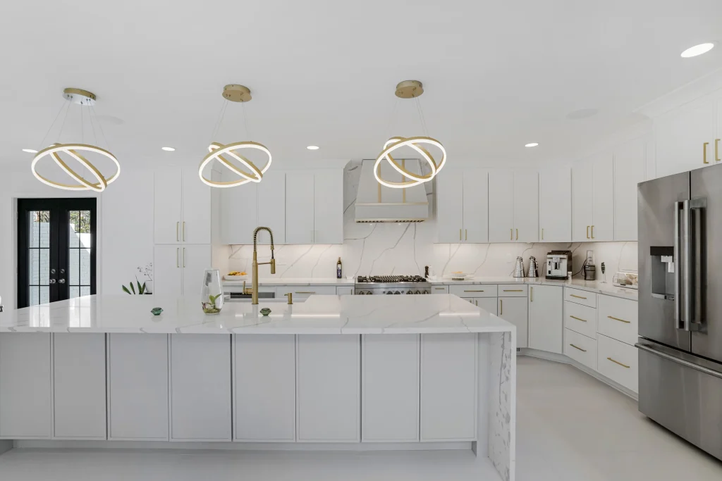 Modern kitchen with white cabinets, gold handles, a large island, marble countertops, stainless steel appliances, and three circular pendant lights hanging from the ceiling.