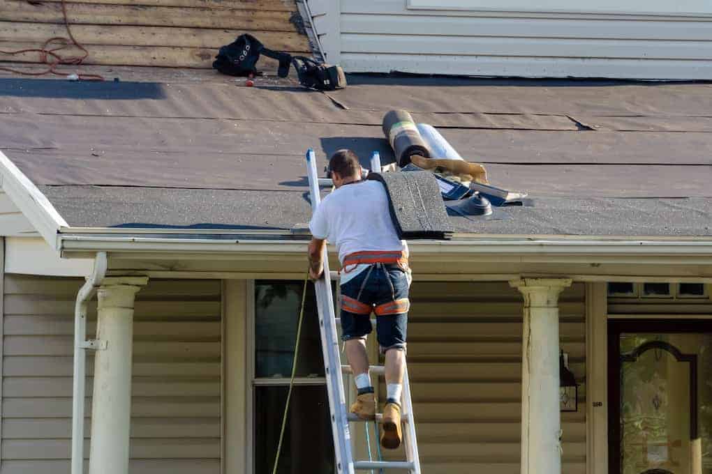 man climbing up ladder with asphalt shingles; diy roof replacement