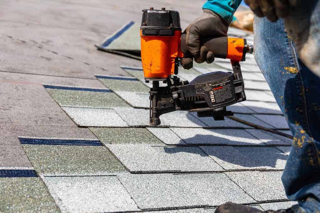 worker installing asphalt shingles with nail gun; diy roof replacement