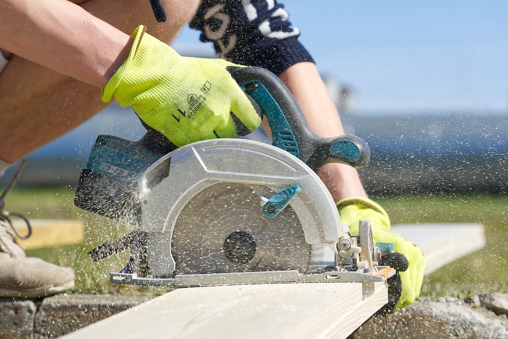 man using circular saw to cut wood; essential roofing tools