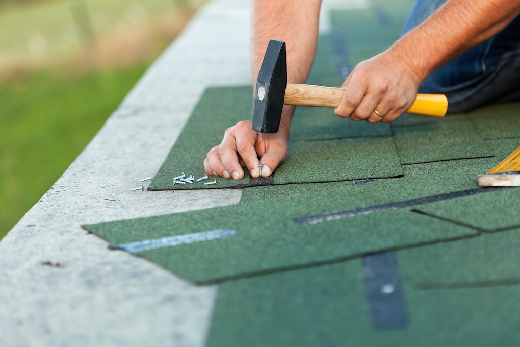 man using roofing hammer to nail shingles; roofing tools