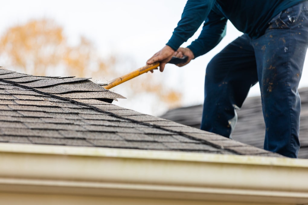 roofer removing shingles with shovel; essential roofing tools