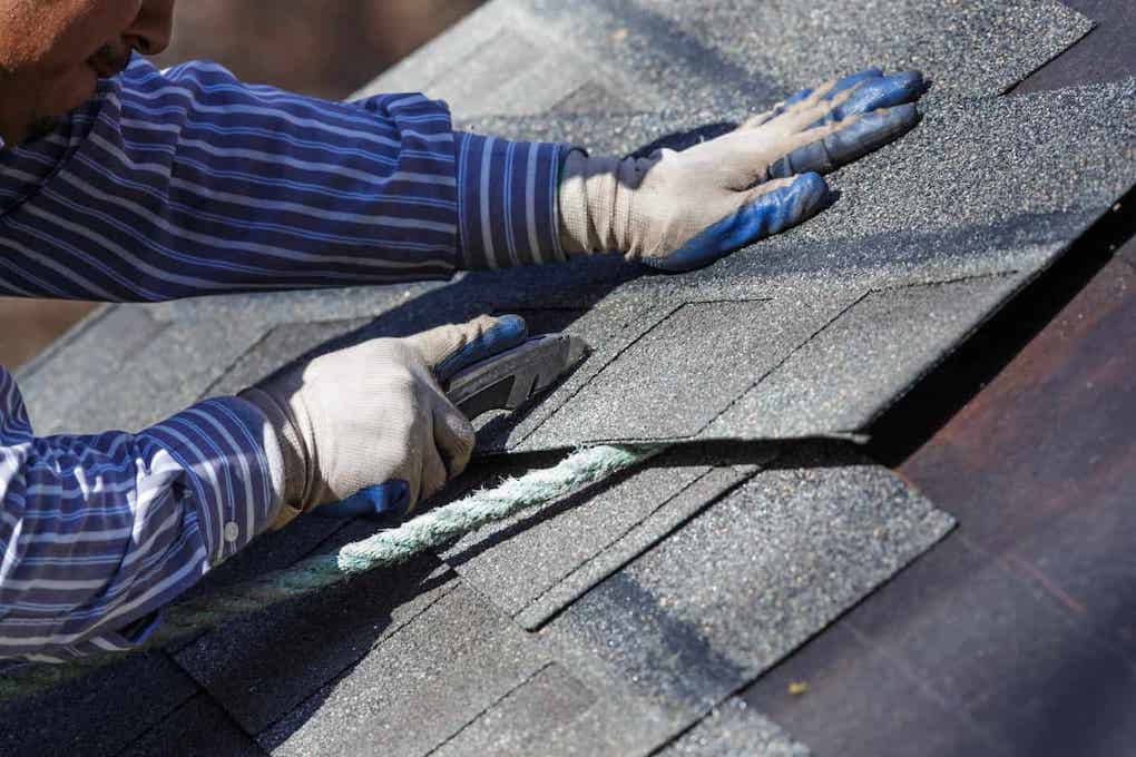 man using utility knife to remove roof shingles; essential tools