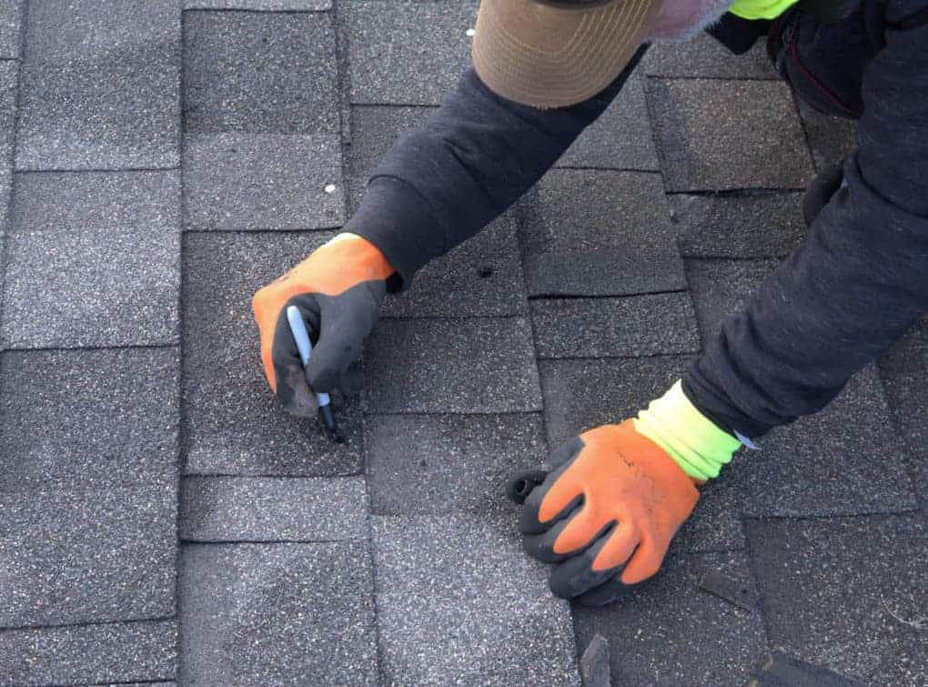 man marking damaged shingles on roof with marker; how to replace shingles that have blown off
