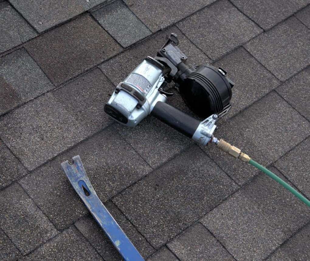 nail gun and pry bar sitting on asphalt shingles; how to replace shingles that have blown off