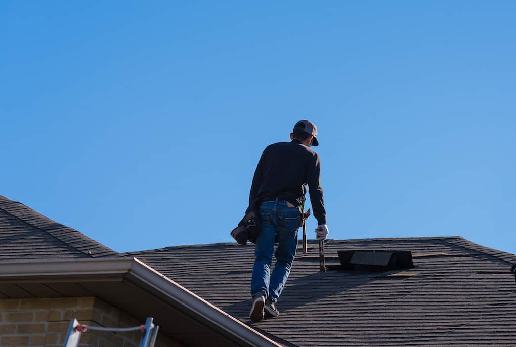 man on top of a damaged roof to assess the damage