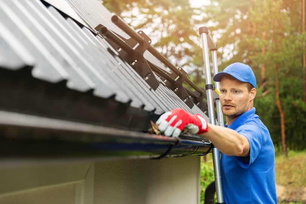 worker with gloves cleaning gutters during professional roof inspection