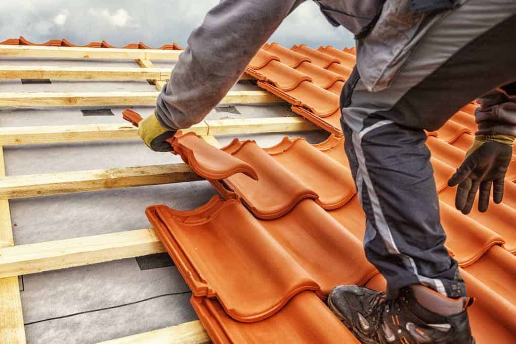 male worker installing clay tiles on roof; roofing companies in fairfax, va