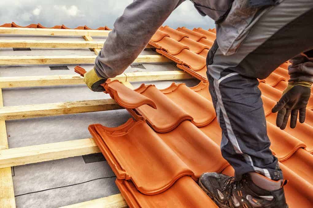 man laying clay roof tiles; roof cleaning guide; roofing materials